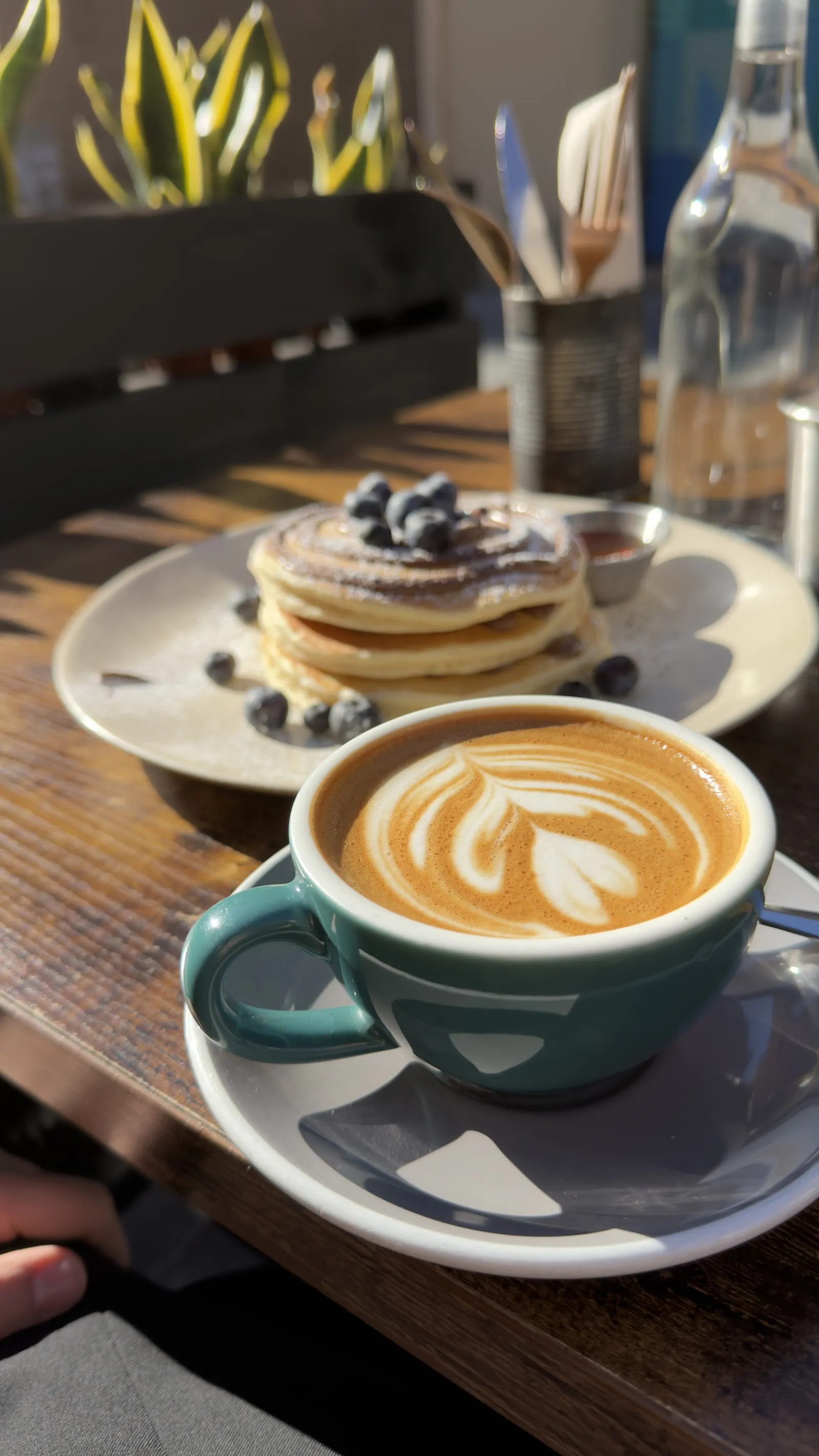 Un latte con arte latte y pancakes con arándanos al fondo