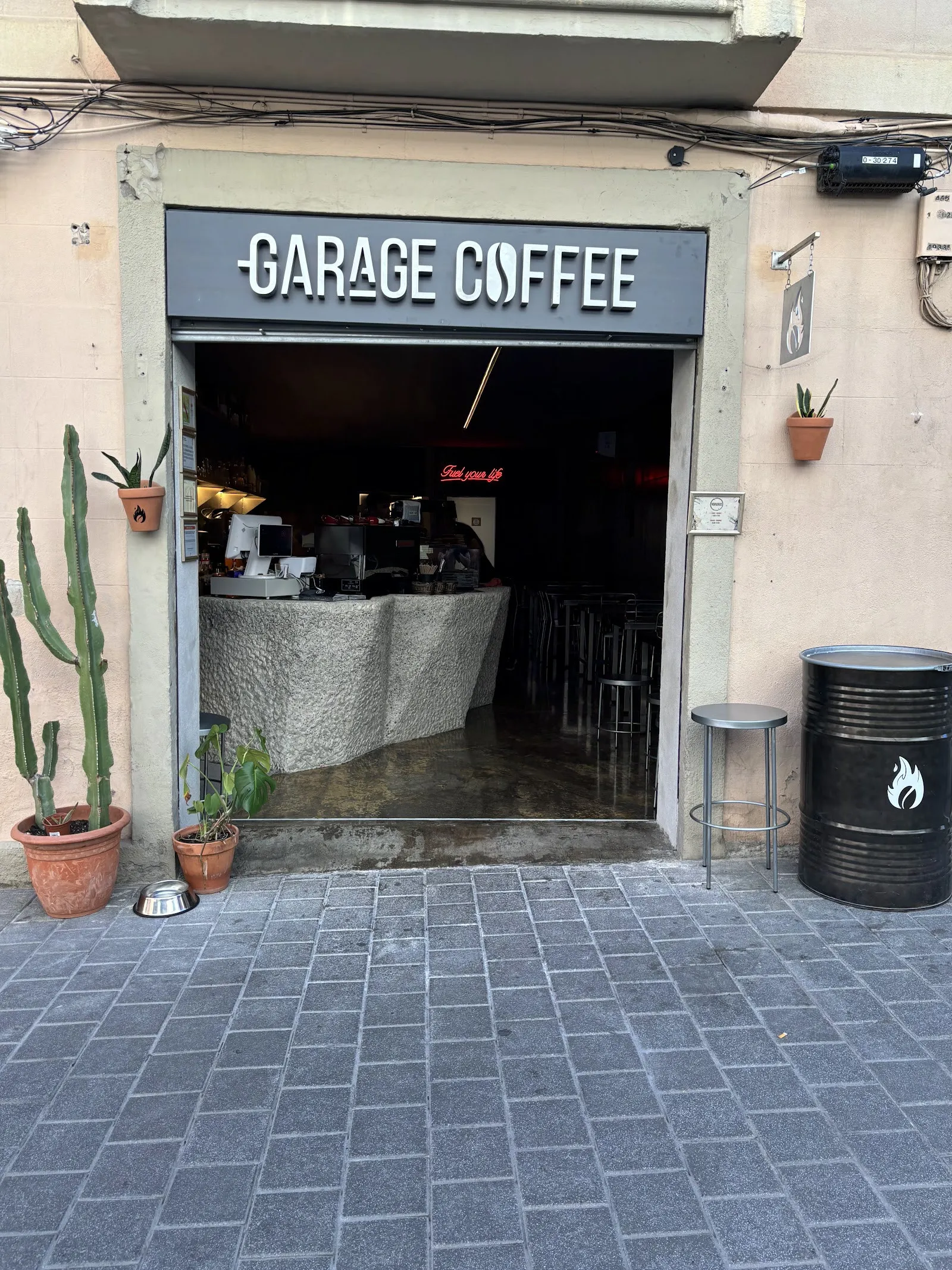 Fachada de Garage Coffee: la puerta de garaje abierta bajo el rótulo, con cactus y plantas en la acera